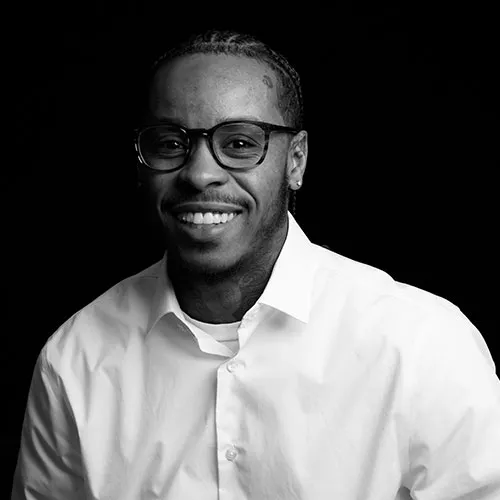 Portrait of Taylor Harvey, founder of Muse Makers, smiling in glasses and a white shirt